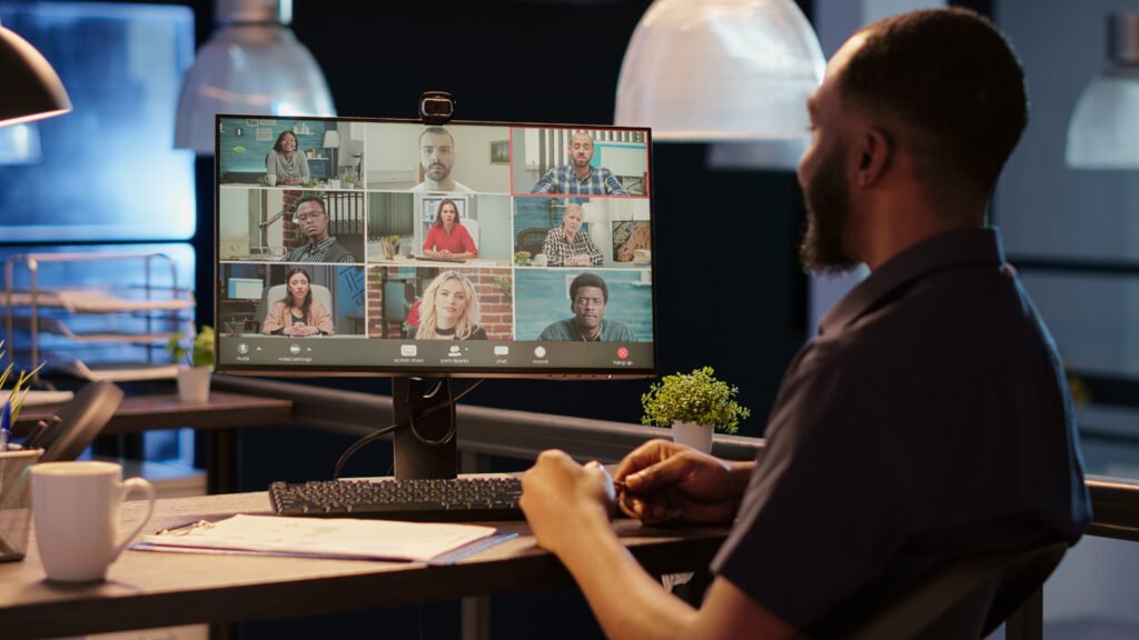 A man is looking at his monitor during an online meeting, having regular check-ins and providing ongoing support to clients.